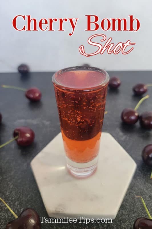 Cherry Bomb Shot over a red cocktail shot on a white coaster surrounded by fresh cherries