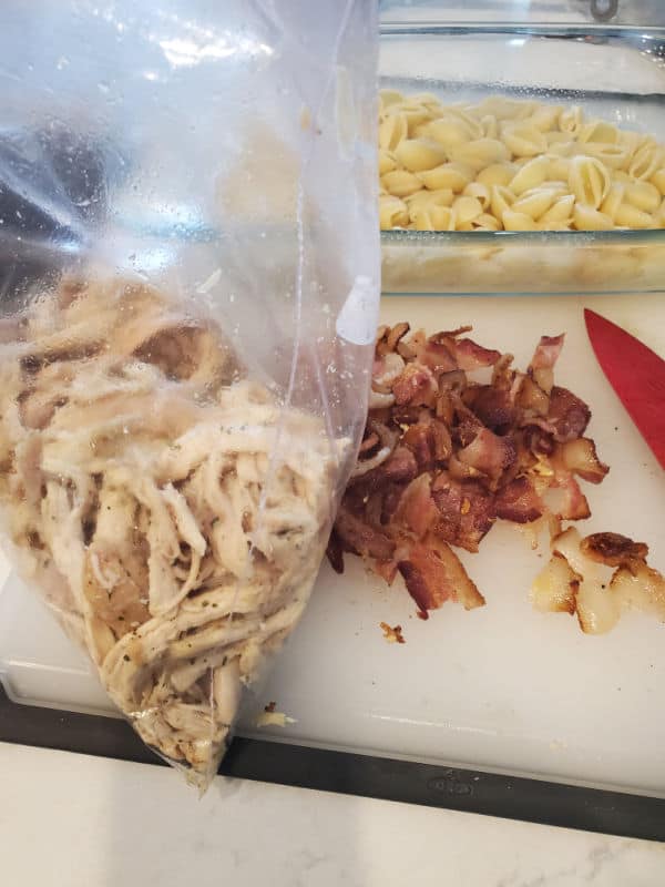 Rotisserie Chicken in a baggie, chopped bacon, next to a casserole dish with pasta shells