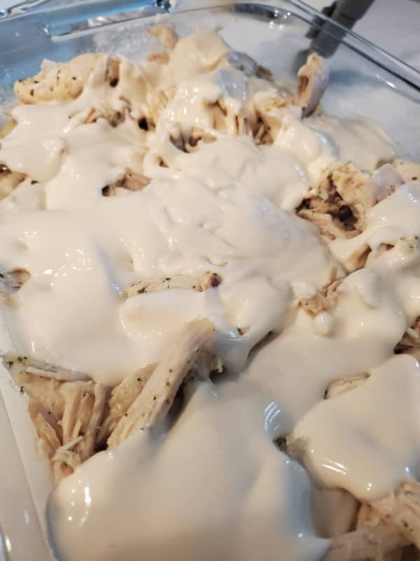 Alfredo sauce over seasoned chicken in a glass casserole dish