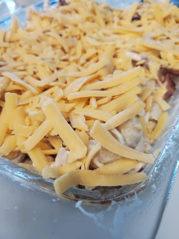 Shredded cheese over chicken and pasta in a casserole dish