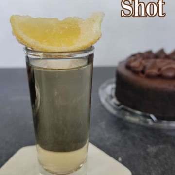Chocolate Cake Shot text over a shot glass with a lemon wedge and a chocolate cake in the background