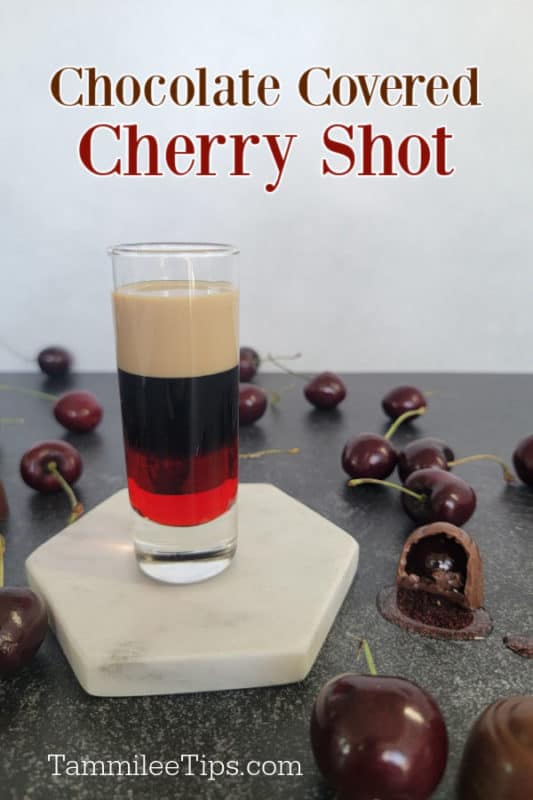 Chocolate covered cherry shot over a layered shot on a white coaster surrounded by chocolate covered cherries