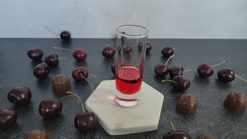 grenadine in the bottom of a shot glass on a white coaster surrounded by chocolate covered cherries