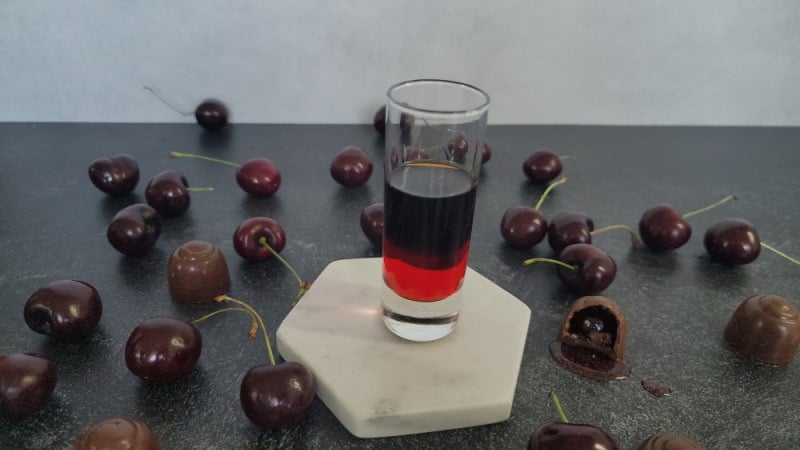 layered drink in a glass shot glass next to chocolate covered cherries