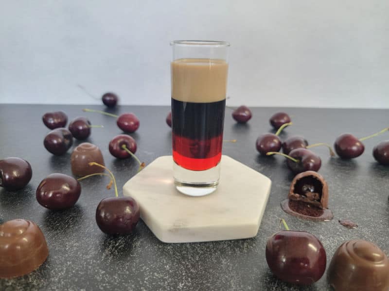Chocolate Covered Cherry Shot on a white coaster surrounded by chocolate covered cherries