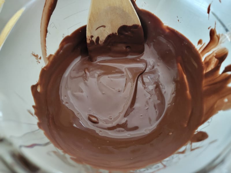 melted chocolate in a glass bowl with a wooden spoon for chocolate covered potato chips