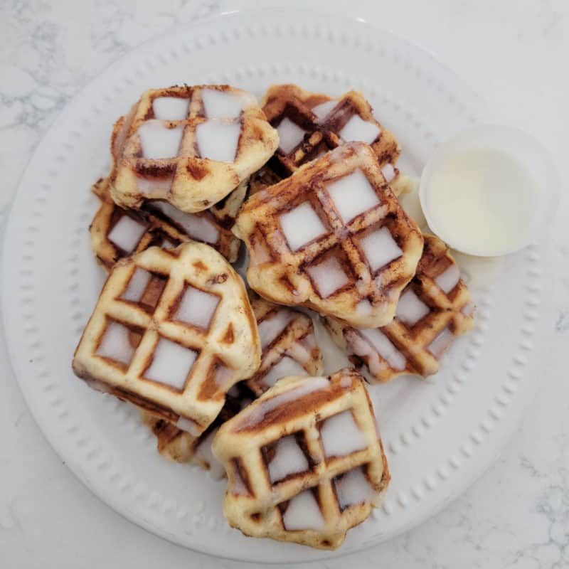 Stack of Cinnamon Roll waffles covered in icing on a white plate