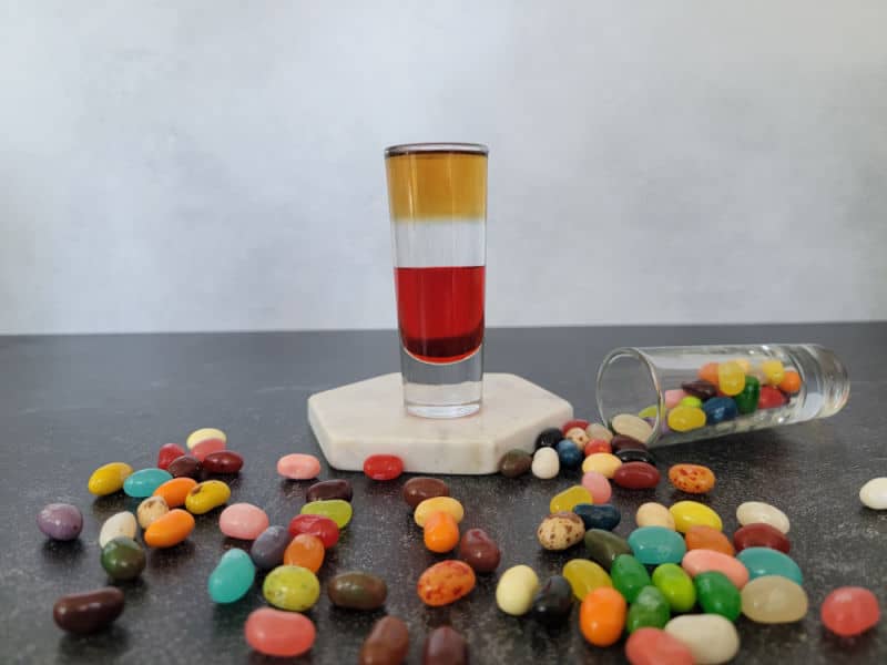 Layered jelly bean shot on a white coaster surrounded by jelly bean candies