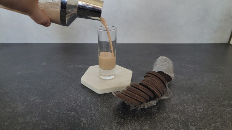 Cocktail shaker pouring into a cocktail glass next to a sleeve of thin mint cookies