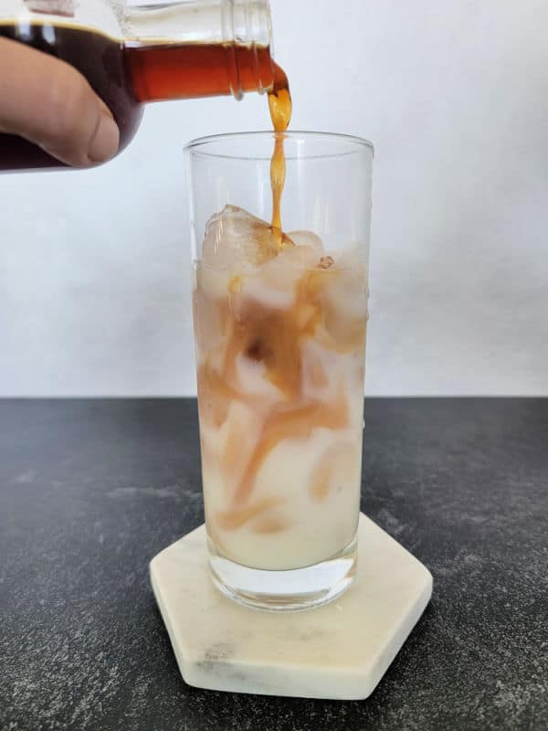 Chai concentrate pouring over milk in a tall glass