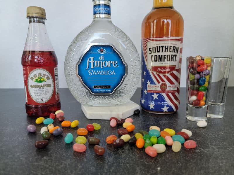 Rose's Grenadine Bottle, Sambuca and Southern Comfort Bottles next to two shot glasses surrounded by jelly beans