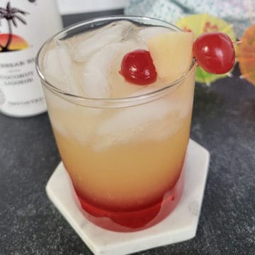 Malibu sunset drink in a clear glass garnished with maraschino cherries and pineapple chunk
