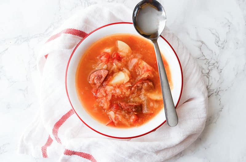 Sausage sauerkraut soup in a white bowl with a spoon on it. 