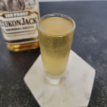 Snakebite Shot on a white coaster next to a bottle of Yukon Jack