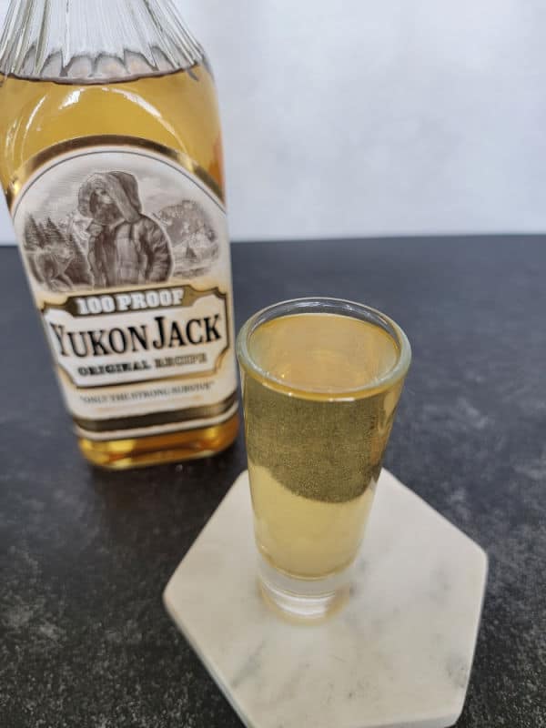 Snakebite Shot on a white coaster next to a bottle of Yukon Jack