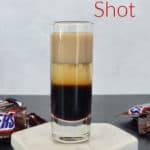 Snickers Shot text over a layered snickers shot on a coaster with Snickers Candy Bars