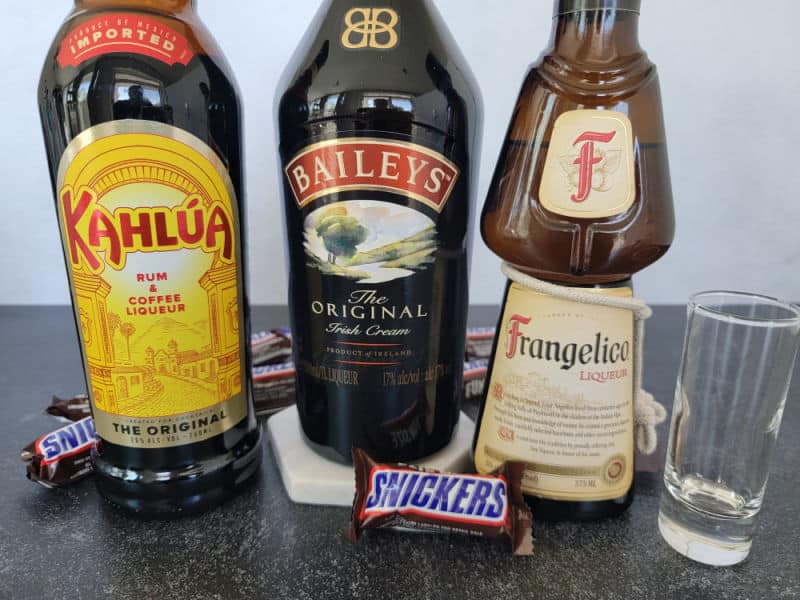 Bottles of Kahlua, Bailey's Irish Cream, and Frangelico next to an empty shot glass