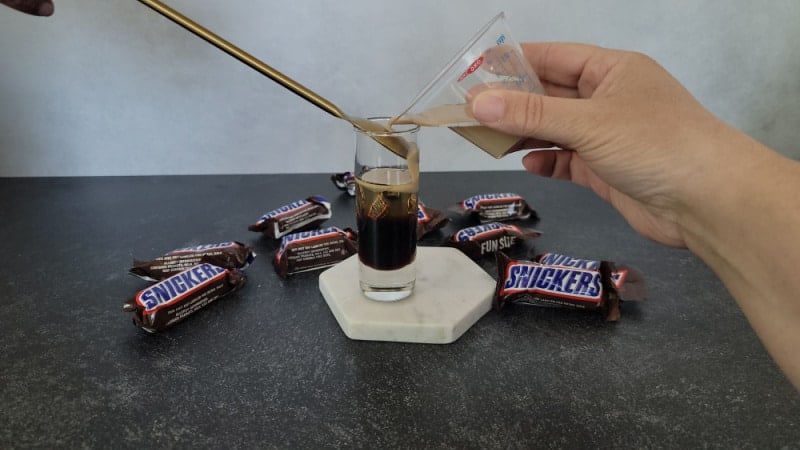 Baileys pouring over a bar spoon to create layers in a snickers shot