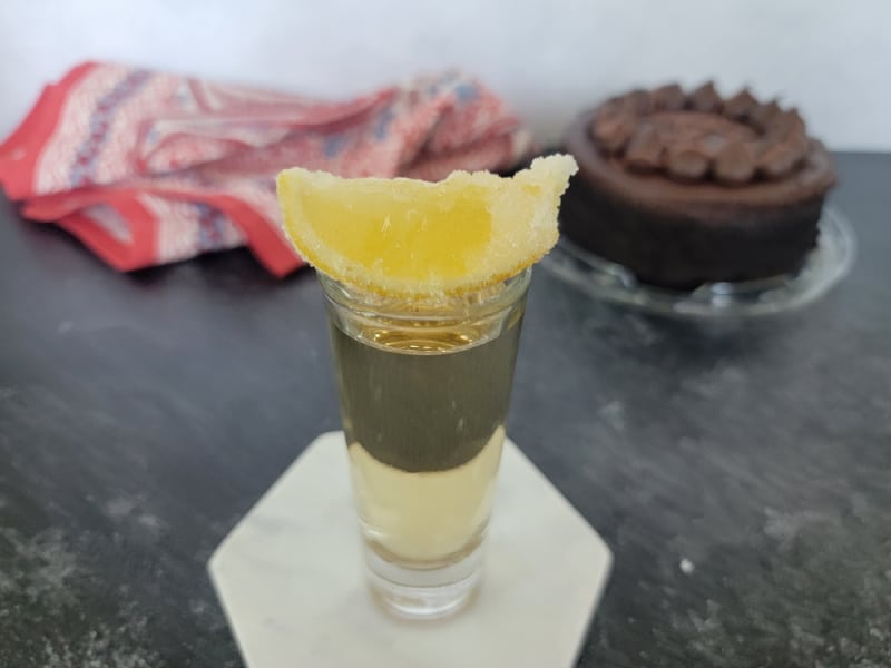 sugar coated lemon on a shot glass on a white coaster in front of a chocolate cake. 