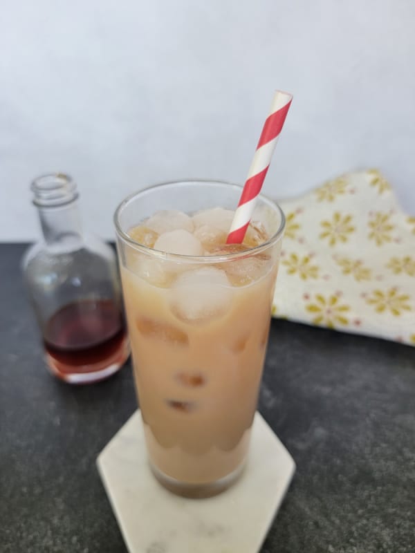 Iced Chai Tea Latte in a tall glass with a striped straw next to a bottle of chai concentrate 