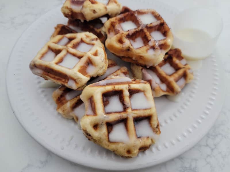 cinnamon roll waffles on a white plate covered in icing 