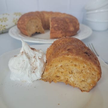 Slice of angel food cake next to whipped cream with a cake in the background