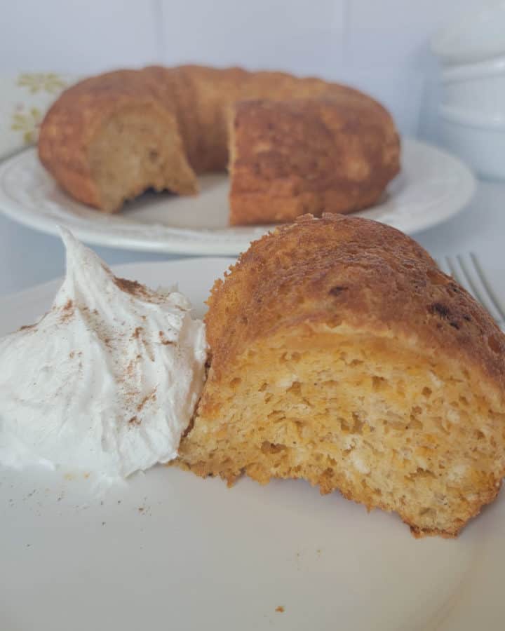Slice of angel food cake next to whipped cream with a cake in the background