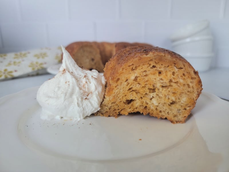 Slice of pumpkin angel food cake next to a dollop of whipped cream on a white plate