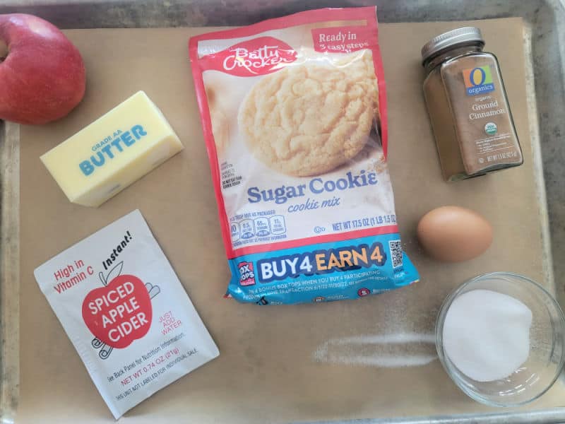 Apple Cider Cookies ingredients, apples, butter, sugar cookie mix, apple cider mix, cinnamon, egg, and sugar on a parchment lined baking sheet