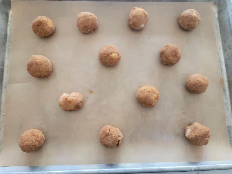 Raw apple cider cookie dough balls on a parchment lined baking sheet