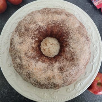 Apple Cider Donut Cake on a white plate with apples next to it