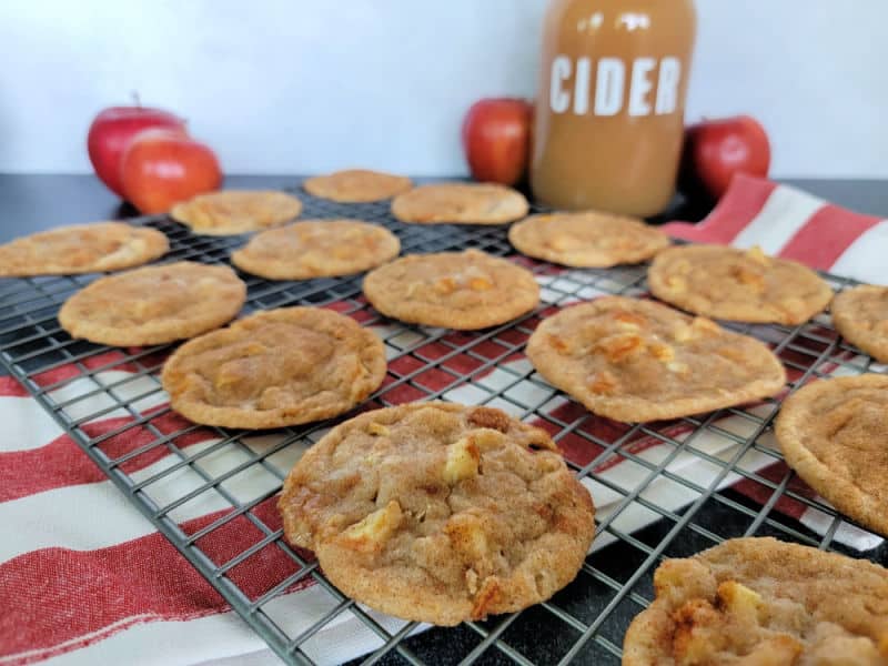 Apple Cider Cookies on a wire rack over a red striped cloth napkin with a jug of apple cider and apples in the background