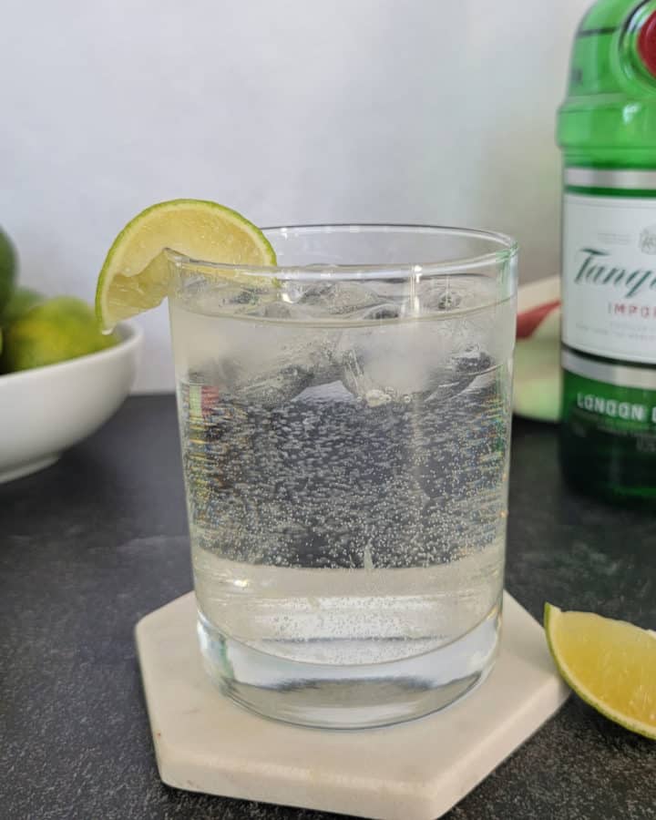 Gin and Sprite cocktail garnished with a lime slice next to a bowl of limes