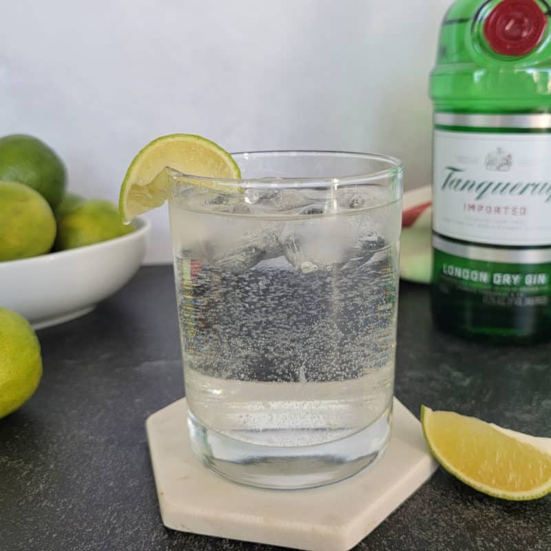 Gin and Sprite cocktail garnished with a lime slice next to a bowl of limes