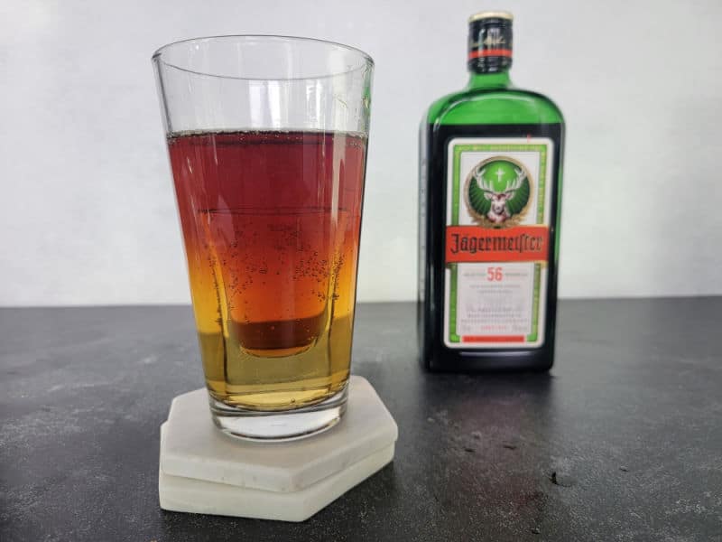 Jager Bomb Cocktail with a shot inside a clear glass next to a bottle of Jägermeister 