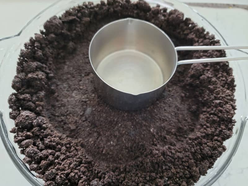 measuring cup pressing an Oreo Crust into a pie dish