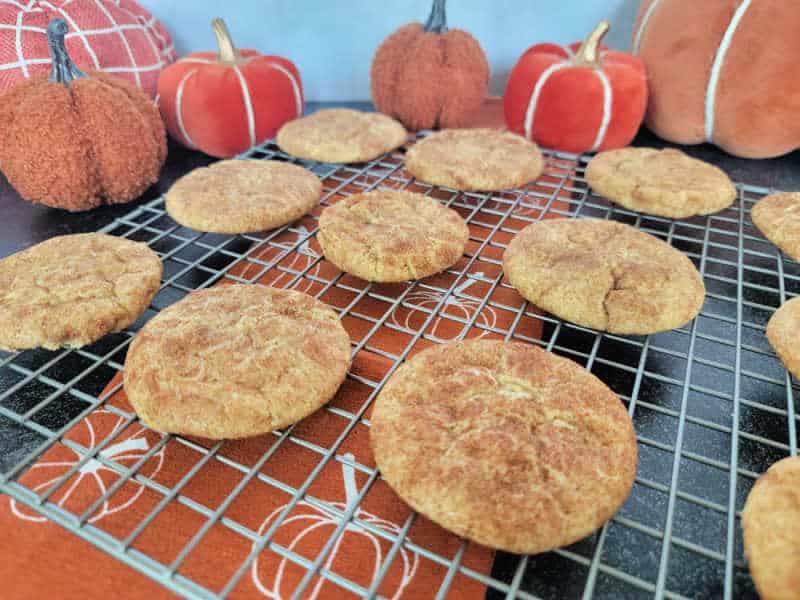 Pumpkin Snickerdoodles on a wire rack over a pumpkin napkin with cloth napkins in the background