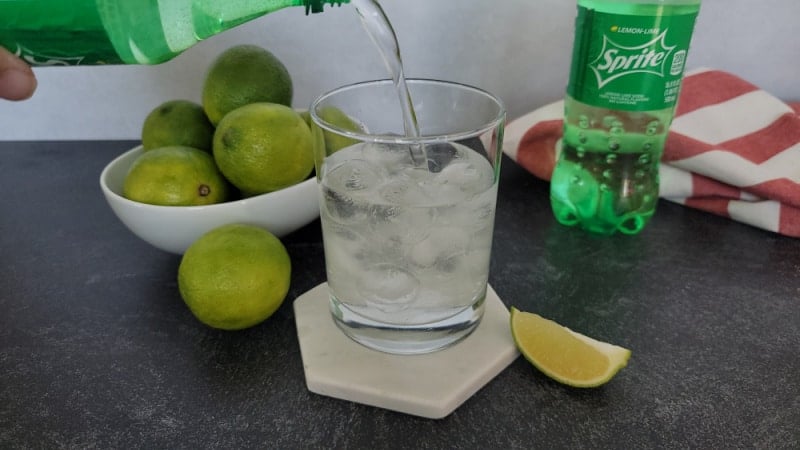 Sprite pouring into a cocktail glass next to a bowl of limes