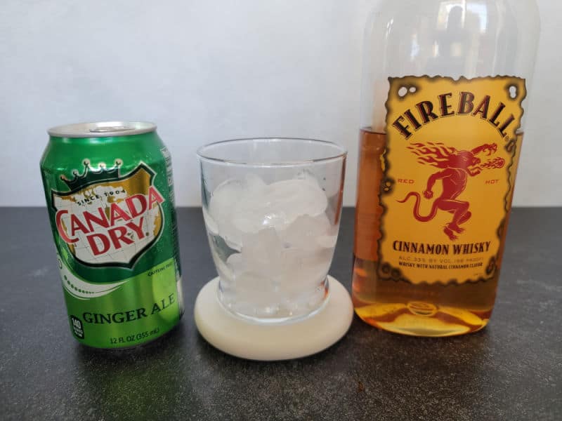 Canada Dry Ginger Ale can, empty glass with ice, and a bottle of Fireball Cinnamon Whisky