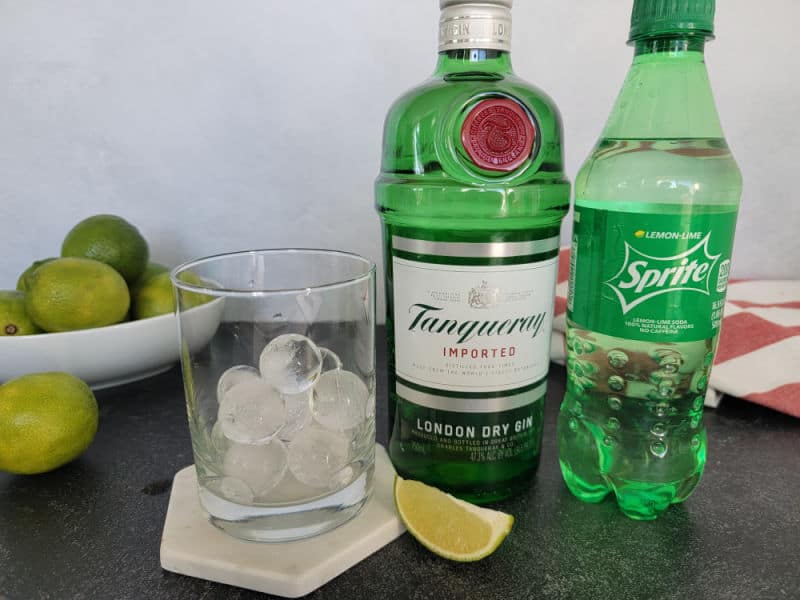 Cocktail glass with ice cubes, Tanqueray Gin, and Sprite by a bowl of limes