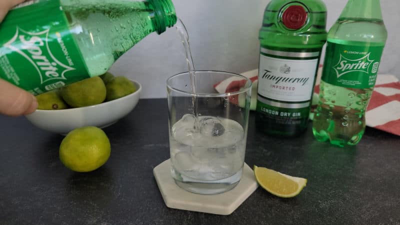Sprite pouring into a cocktail glass next to a bottle of gin and Sprite