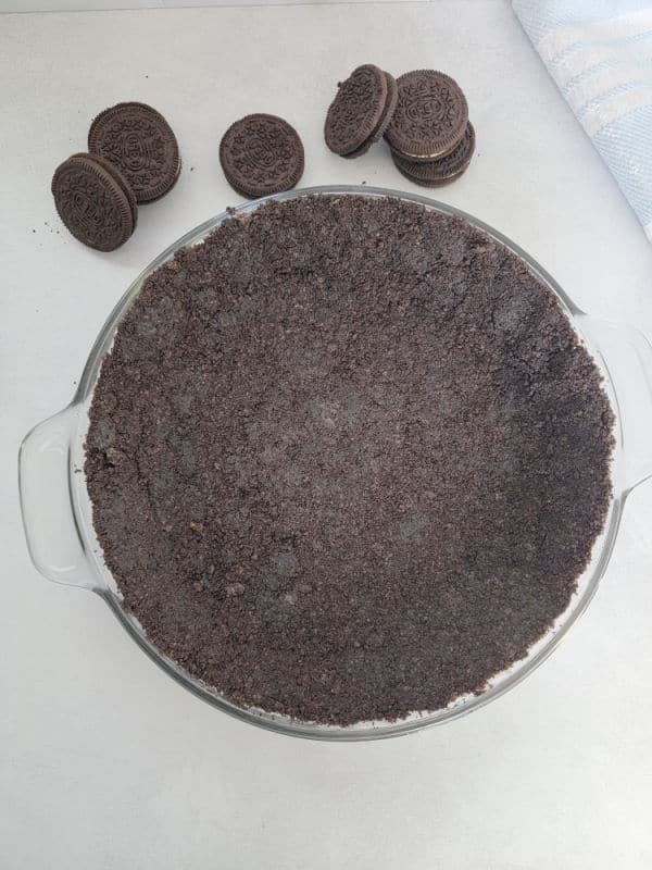 Oreo Crust in a pie dish with a couple of Oreo Cookies and a blue napkin