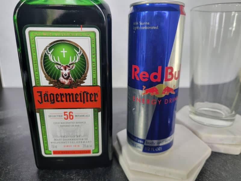 Jägermeister bottle next to a can of Red Bull and an empty glass for a Jager Bomb Shot