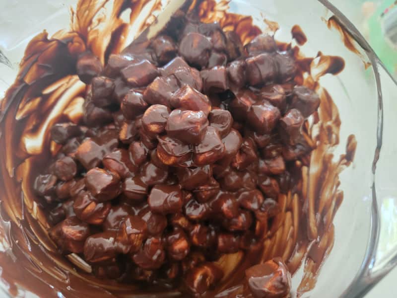 Marshmallows coated in milk chocolate in a glass batter bowl for no bake church window cookies