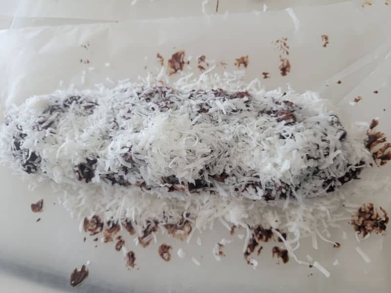 Coconut covering chocolate and marshmallows in a log shape for no bake church window cookies on parchment paper. 