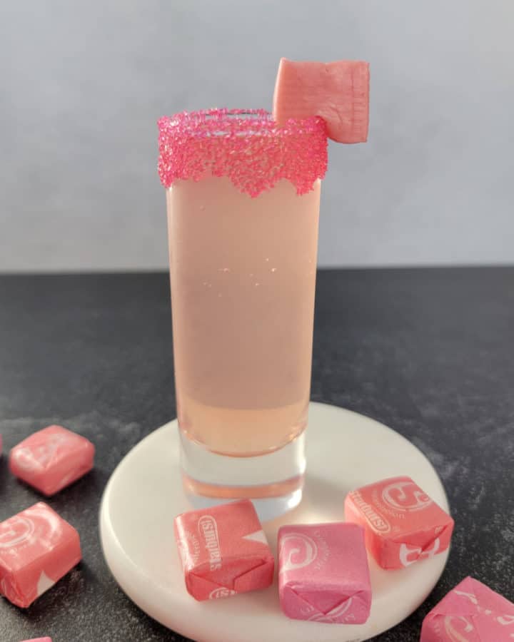 Pink Starburst Shot on a white coaster surrounded by Starburst candies