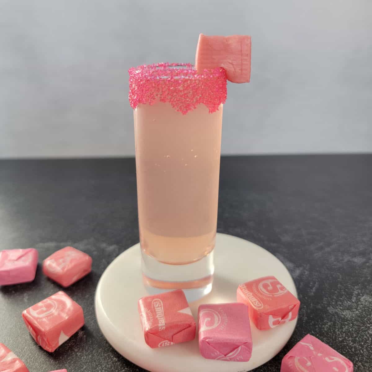 Pink Starburst Shot on a white coaster surrounded by Starburst candies