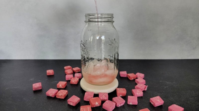 Sour watermelon pouring into a mason jar surrounded by pink starburst candies