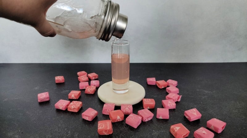 mason jar cocktail shaker pouring a pink starburst shot into a shot glass