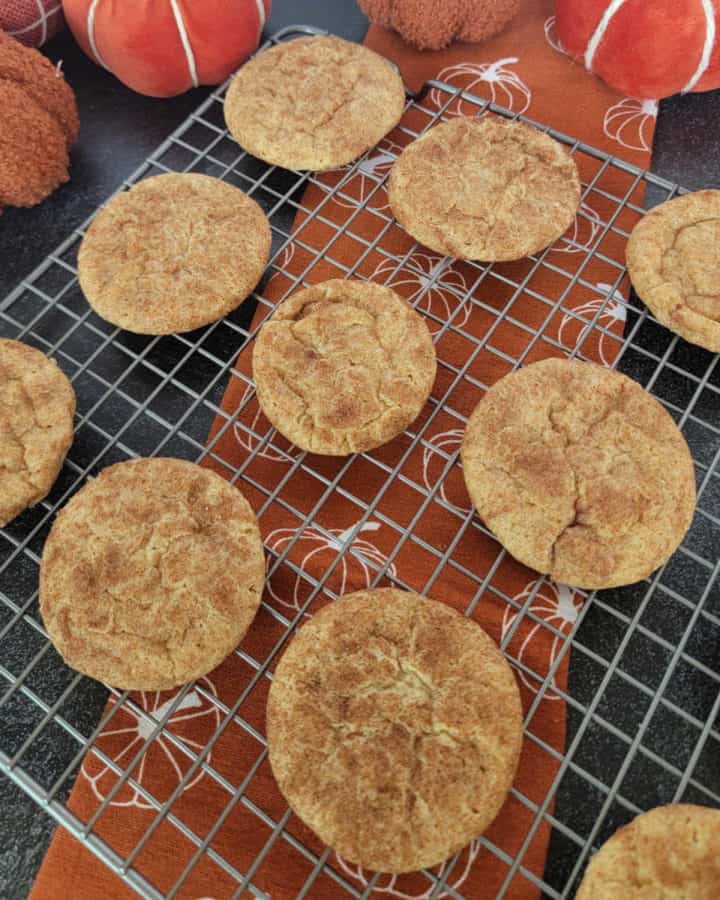 Pumpkin Snickerdoodles on a wire rack over a pumpkin napkin with cloth napkins in the background